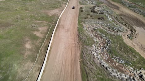 Following-a-4x4-car-with-a-drone-on-a-dirt-road,-dramatic-angle