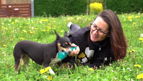señora tumbada en el césped jugando con un perro de rescate y un juguete chirriante, morena de pelo largo