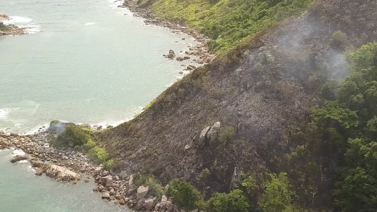 해안 산의 일부가 불에 타고, 식물에서 나오는 연기가