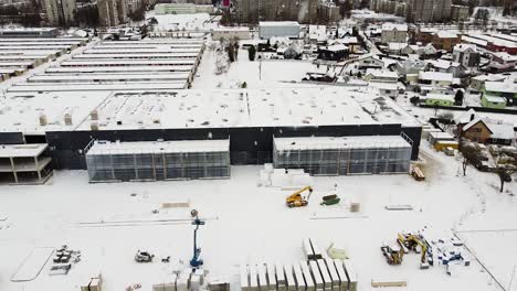 modern logistic building construction site with kaunas city behind during heavy snowfall, aerial side fly view