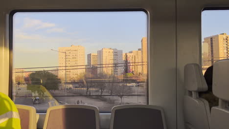 through train window, towering city houses illuminated by evening sun, set against canvas of clear sky