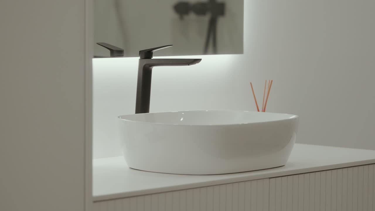 Beyaz tezgah üstü lavabo ve siyah musluklu minimal banyo iç mekanı