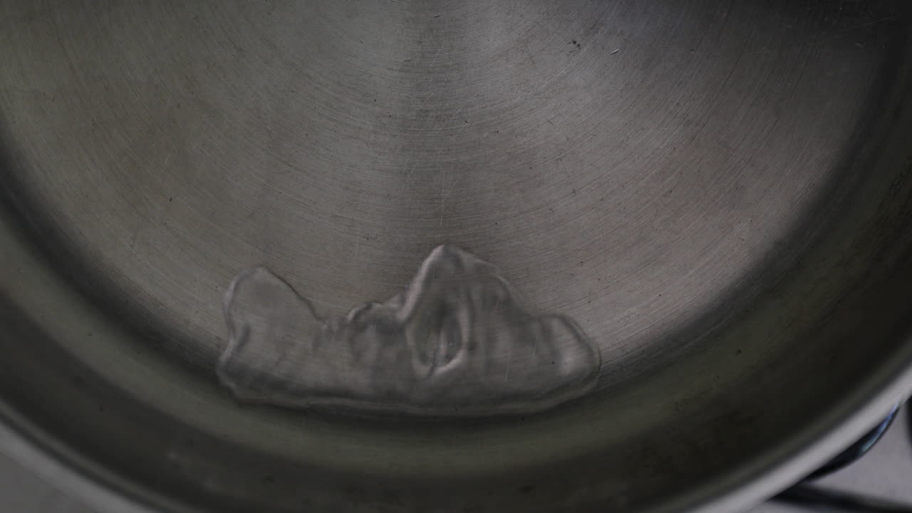Vista al rallentatore dell'acqua che spruzza in una padella di acciaio inossidabile e si unisce con un movimento semicircolare.