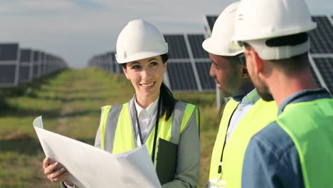 close-up view of three multiethnics farm solar engineers talking while looking at blueprint on solar plantation