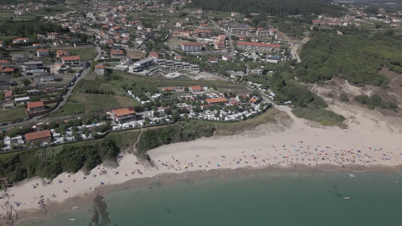 Filmagem aérea bruta de uma vila costeira com uma praia imensa e águas cor de esmeralda.