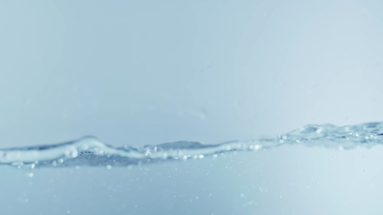 슬로우 모션의 깨끗한 물 표면은 물이 튀는 상점으로 화면을 채우고 기포로 액체 표면을 흔들고 있습니다.