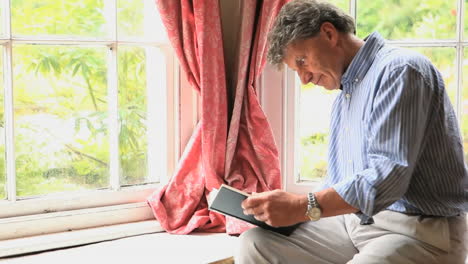 Mature-man-sitting-by-a-window-reading-a-book