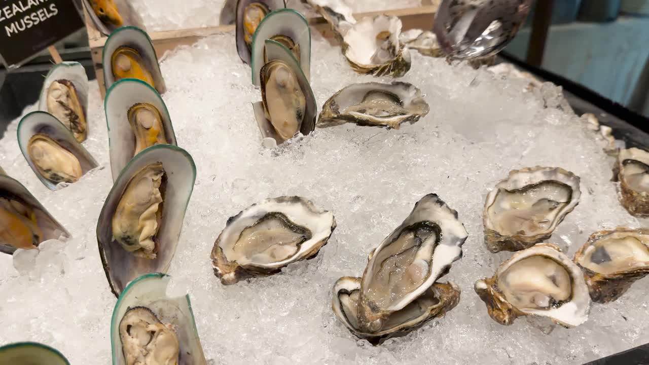Hand uses spoon to serve oysters and mussels displayed on crushed ice under bright lighting