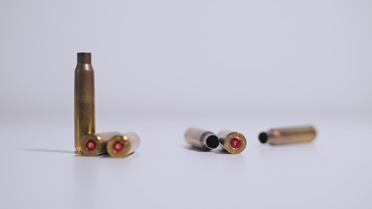An empty rifle cartridge drops among others on white table, dramatic slow motion