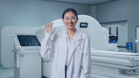 asian woman doctor waving hand and smiling to camera with mri machine in the hospital
