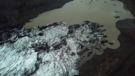 Aerial-landscape-view-over-Sólheimajökull-glacier,-melting-into-water,-during-summer,-in-Iceland