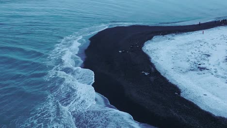 Aerial-view-over-the-shoreline-of-diamond-beach,-covered-in-snow,-at-dusk