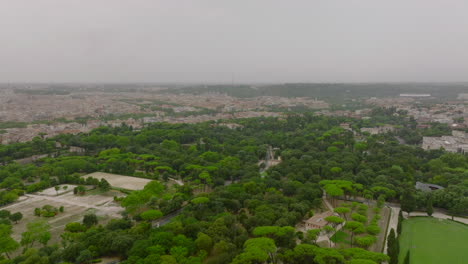 Vista-Panorámica-Aérea-De-La-Gran-Ciudad-En-Un-Día-Nublado.-Adelante-Vuela-Sobre-El-Parque-Con-árboles-Verdes-Y-Complejo-Ecuestre.-Roma,-Italia