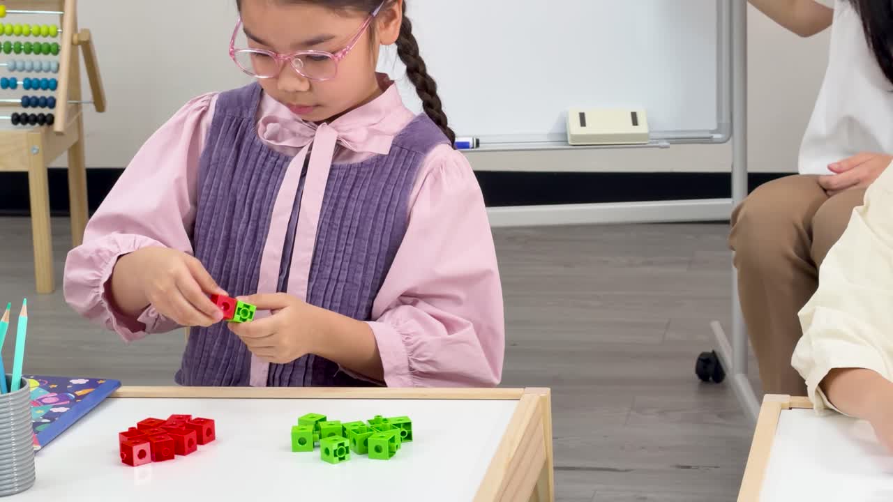 Girl uses colorful math cubes for hands-on learning in bright, modern classroom with teacher observing