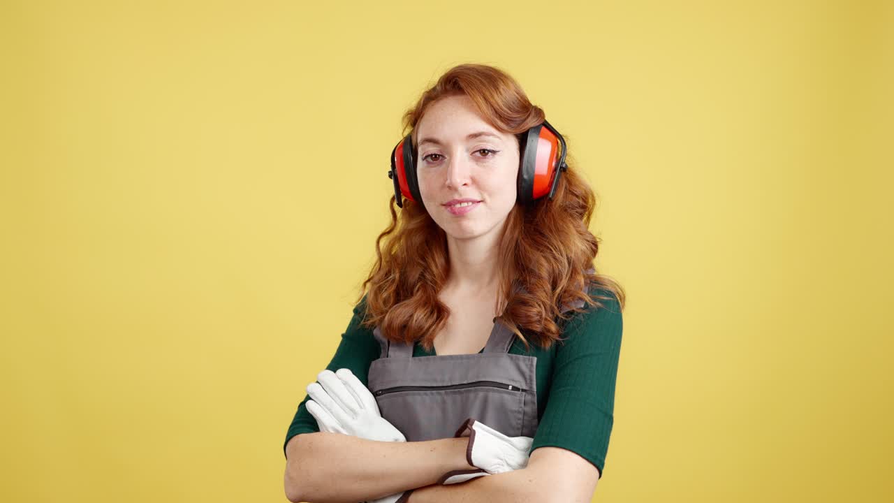 Redhead woman in work overalls, earmuffs, and gloves