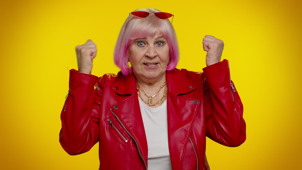mujer con chaqueta de cuero roja con cabello rosado y gafas de sol apuntando