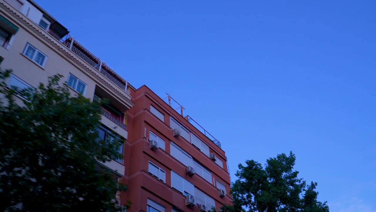 Una ripresa a mano libera dal basso che cattura la facciata di tradizionali edifici residenziali spagnoli contro un cielo crepuscolare limpido e blu a Madrid.