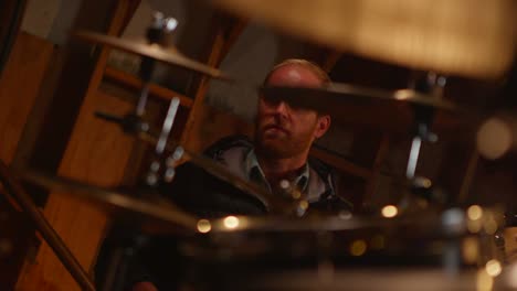 a musician plays as seen through a set of drums being played in the foreground