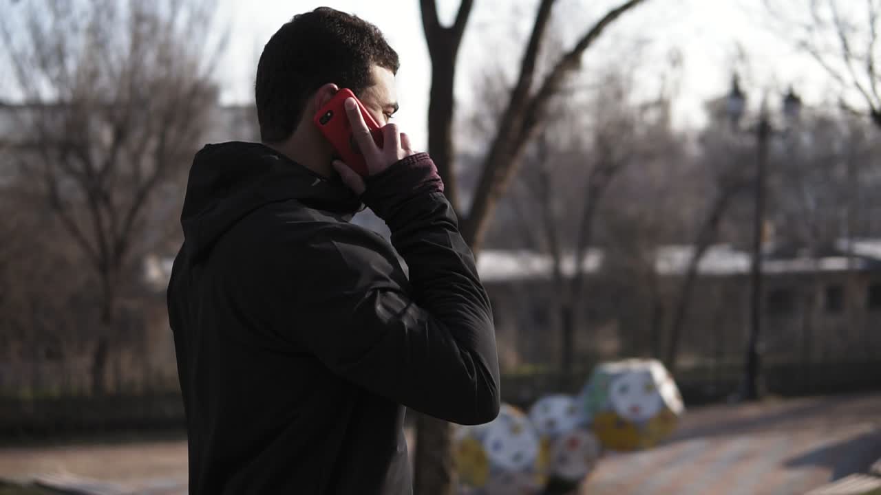 공원에서 걸어서 누군가와 전화로 얘기하는 알아보기 힘든 남성.