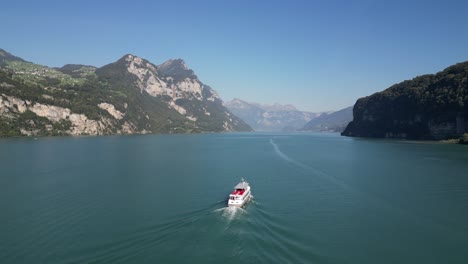 drone view of a white ship cruising across blue waters at the base of a beautiful mountain range