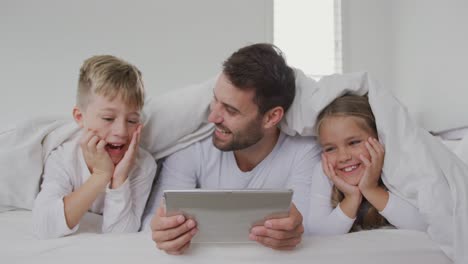 Father-and-children-using-digital-tablet-under-blanket-on-bed-at-home-4k