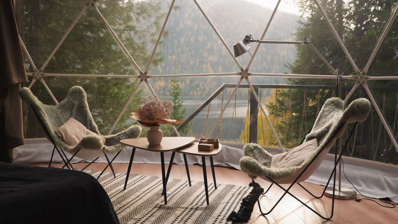 커피 테이블과 의자와 함께 유리 테라스. 호수와 숲의 멋진 전망을 즐기기 위해 점심 휴식을 위해 아한 가구와 함께 글램핑 하우스의 파노라마 발코니