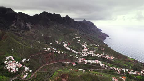 Aerial-of-coastal-tropical-town-surrounded-by-green-mountain,-Tenerife