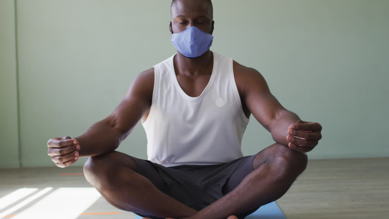 hombre afroamericano en forma con máscara practicando yoga en el estudio de yoga