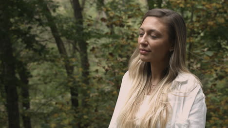 young woman standing in a forest looking up at trees on a late summer day