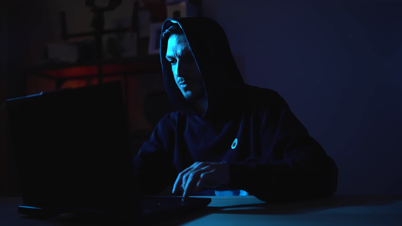 Cyber Intrusion and Data Breach Concept – Hacker in Mask and Hoodie Typing in the Dark Representing Anonymous Crime and Virus Attacks