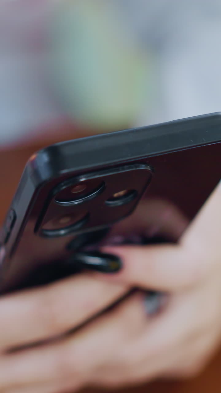 vista borrosa de la mano de la dama con uñas pintadas interactuando con el teléfono inteligente colocado en una mesa de madera, centrándose en la tecnología moderna y la moda en un entorno suave y vibrante con un fondo borroso