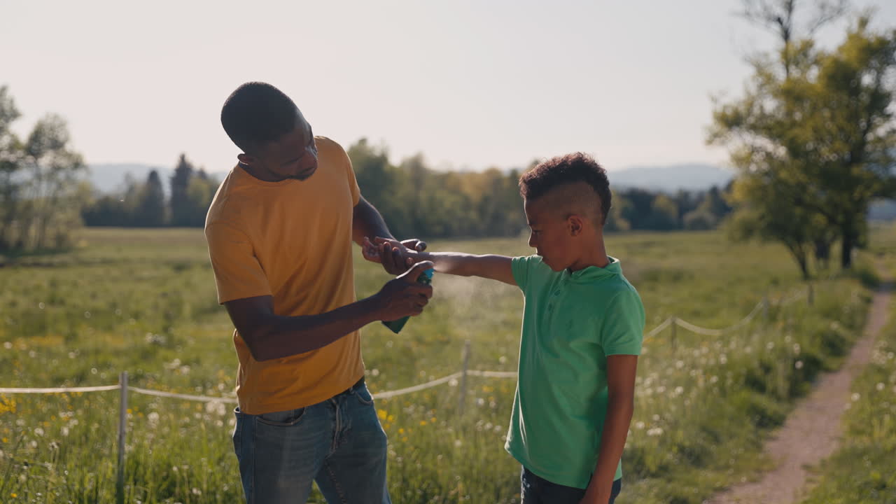 Afroamerikansk mand sprayer et barn med insektspray for at beskytte sin søn mod myg og