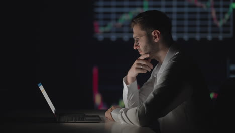 A-professional-with-glasses-looks-at-the-computer-monitor-screen-and-thinks-analyzing-the-securities-market.-Brooding-puzzled-broker-waits-for-the-growth-of-shares