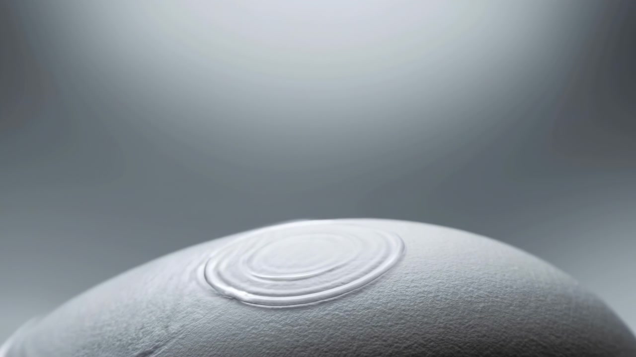 Primo piano da angolazione bassa che mostra una cupola opaca arrotondata con superficie texturizzata e un pulsante circolare concentrico, mentre una luce soffusa dall'alto si sposta sulla parte superiore, creando giochi di luce e ombra mutevoli in un contesto astratto.