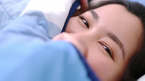 closeup of female smiling and looking at camera and lovely lies in bed covered with blanket