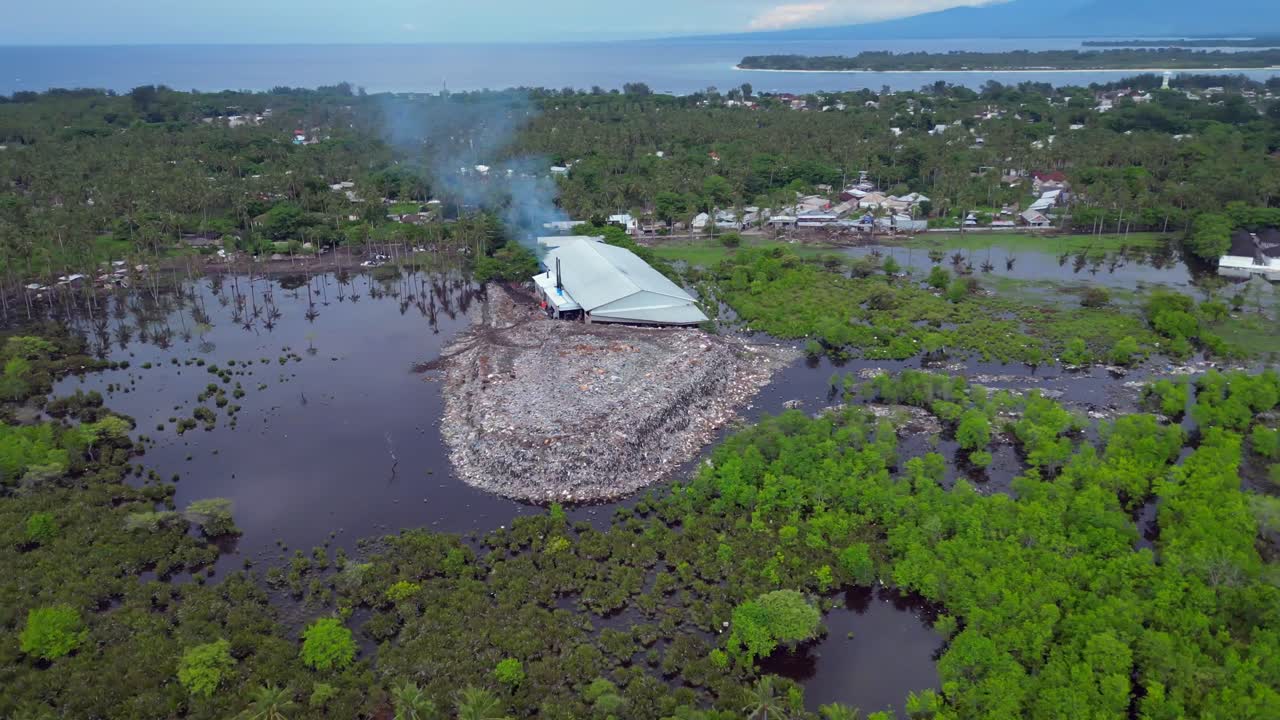 Tempat pembuangan sampah besar menyebar ke air yang tercemar, menunjukkan kerusakan lingkungan, sampah plastik di sebuah pulau di Indonesia. Time-lapse dengan efek gerak super cepat. Pemandangan udara indah, panorama orbit luas.