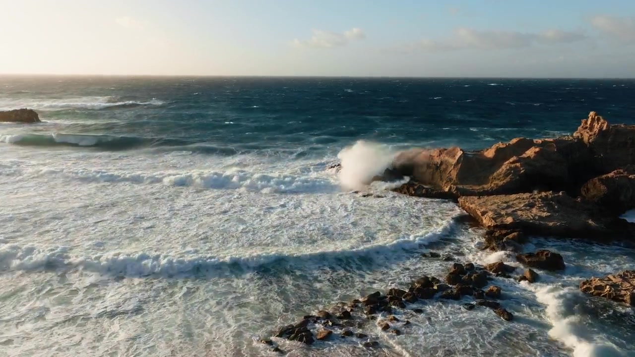 Vista aerea di potenti onde oceaniche che si infrangono su una costa rocciosa.