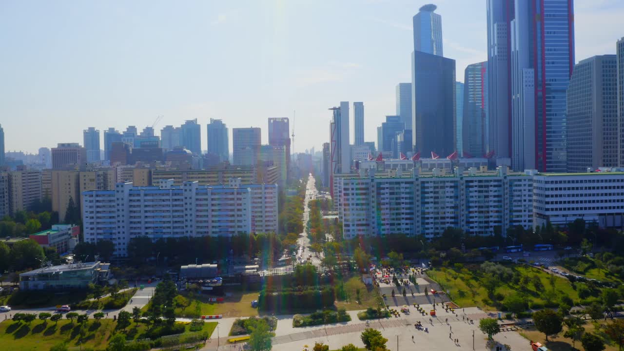 Drone shot traveling forward above a park toward the a residential area and business buildings in Seoul city during a sunny day