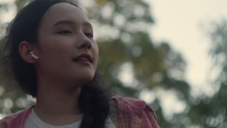 asiatic woman listening in slow motion to playlist pop music summer hit with earphone , travelling tree at sunset in background