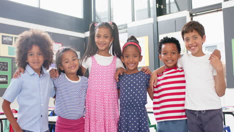 smiling school children standing together in classroom, arms around each other