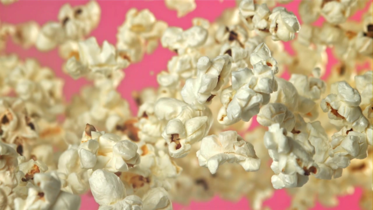Deliciosas palomitas volando en cámara lenta sobre un fondo rosa