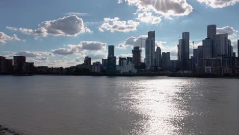 Establishing-shot,-Canary-Wharf-Tall-waterfront-buildings,-Sunlight-reflection-on-Thames-River,-Panning-shot