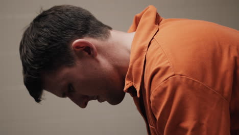 un hombre triste, deprimido atractivo, guapo, prisionero criminal, recluso con mono naranja sentado en una celda pensando, reflexionando, solo