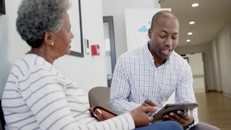 African-american-male-doctor-using-tablet-and-talking-with-senior-woman-in-hospital,-slow-motion