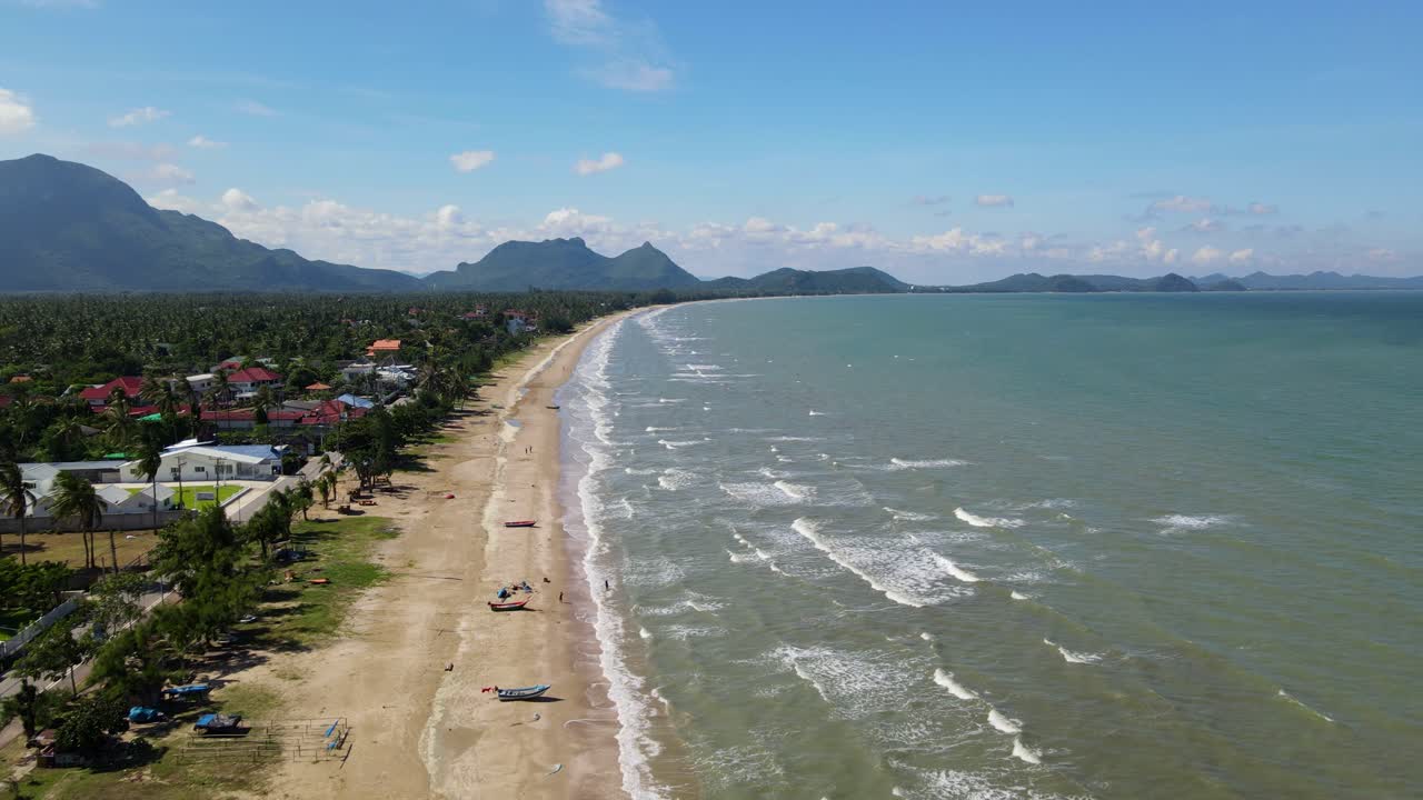 Unas imágenes aéreas inversas revelando la playa con barcos y gente bañándose, un paisaje y cielo preciosos