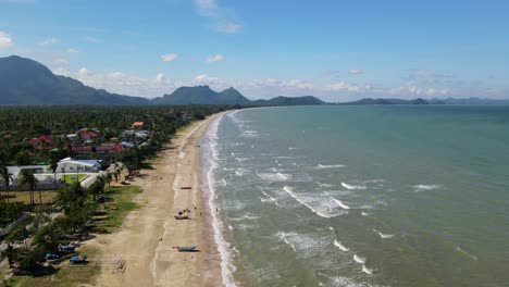 a reverse aerial footage revealing the beach with boats and people bathing, gorgeous landscape and sky