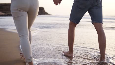 unrecognizable young couple stepping together at the golden sand at sea beach. male and female legs walking near ocean. bare