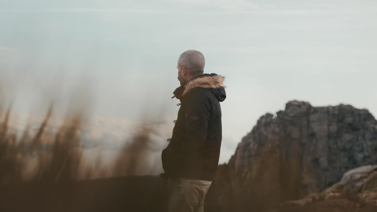 Uomo ispirato che cammina tra le montagne, con le mani in tasca, e viste mozzafiato sull'orizzonte sullo sfondo.