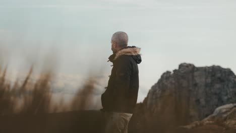 Inspired-man-walking-through-the-mountains,-hands-in-his-pockets,-with-stunning-views-of-the-horizon-in-the-background