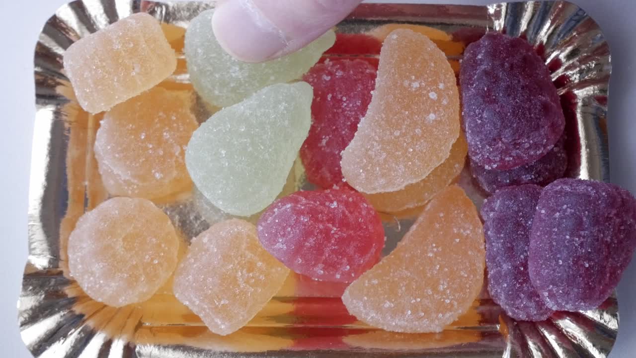 Colorful gummy candies being picked from a tray in bright lighting
